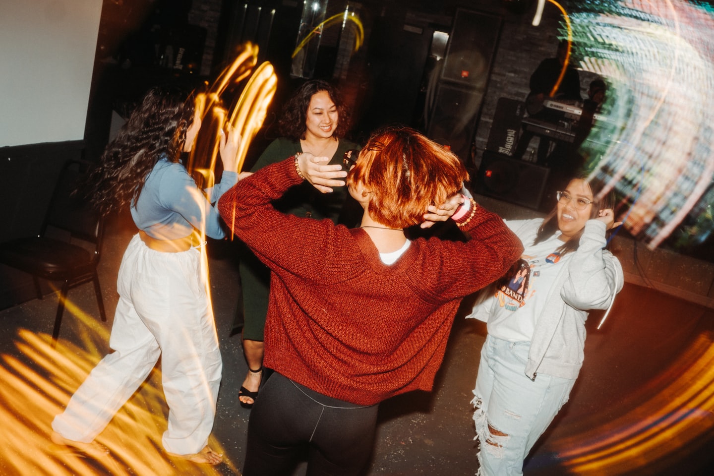 Four adults dancing energetically in a lively venue with light streaks.