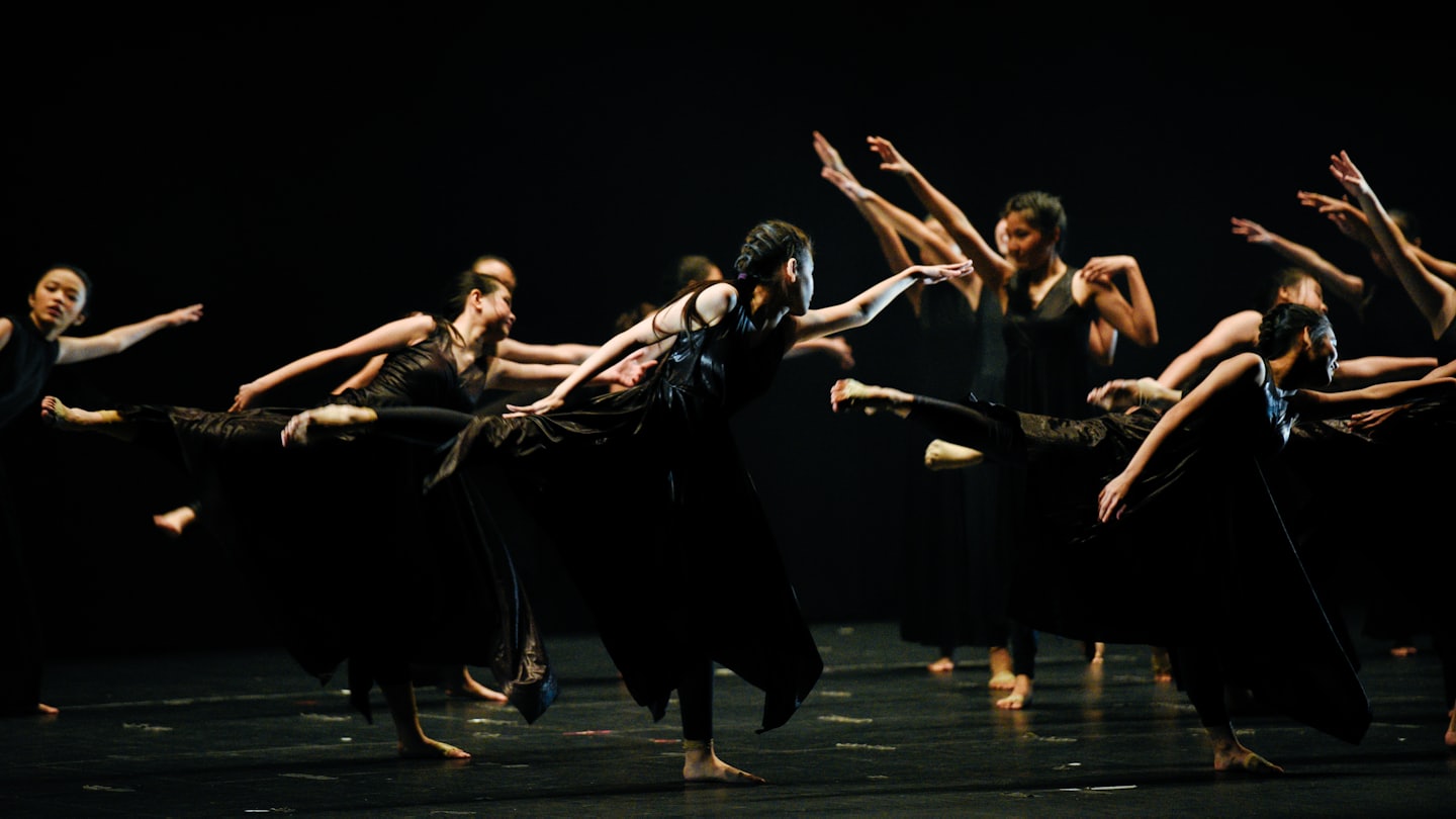 East Asian dancers in black costumes perform a contemporary routine.