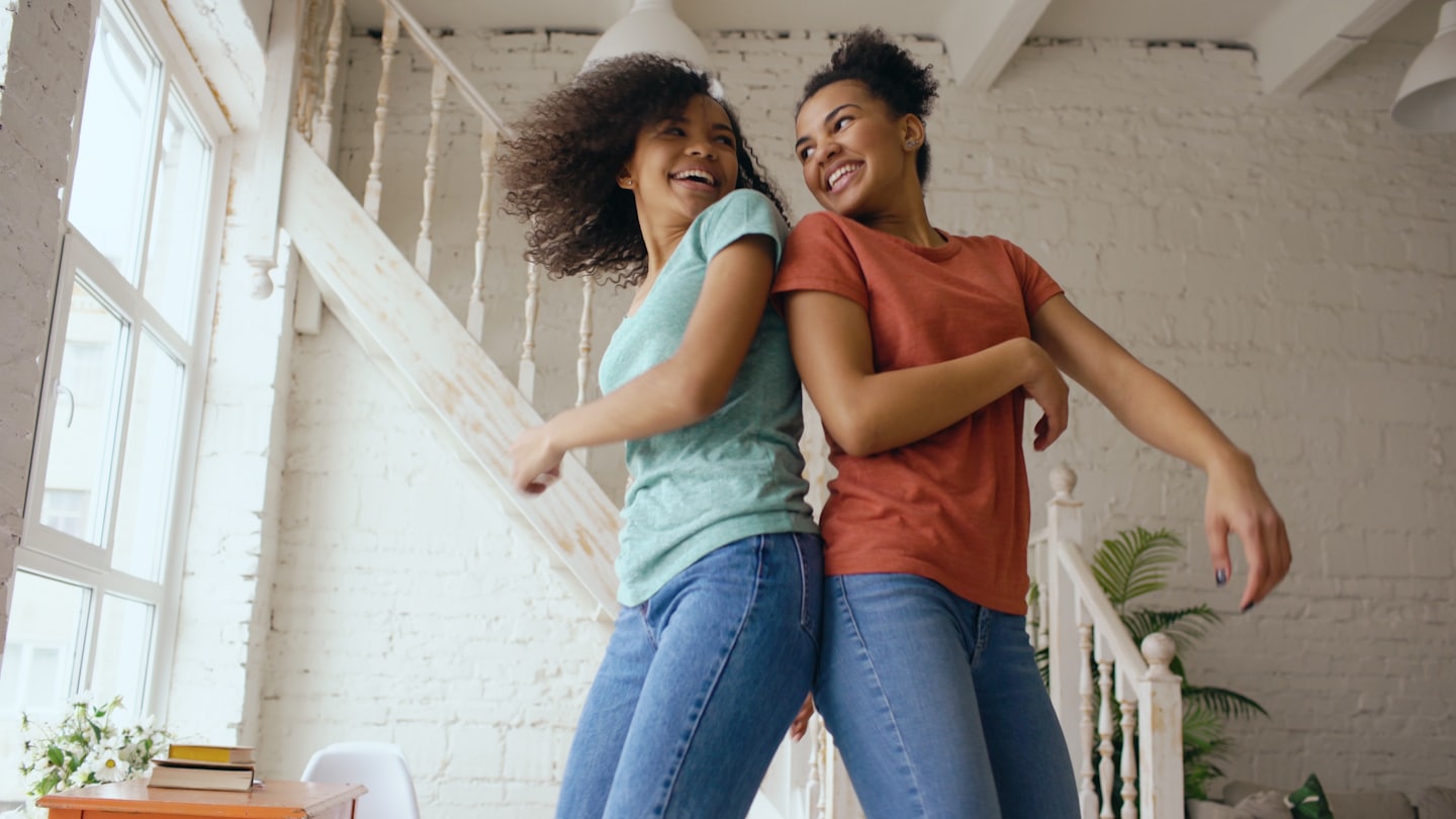 Two women laugh and dance while standing back to back.